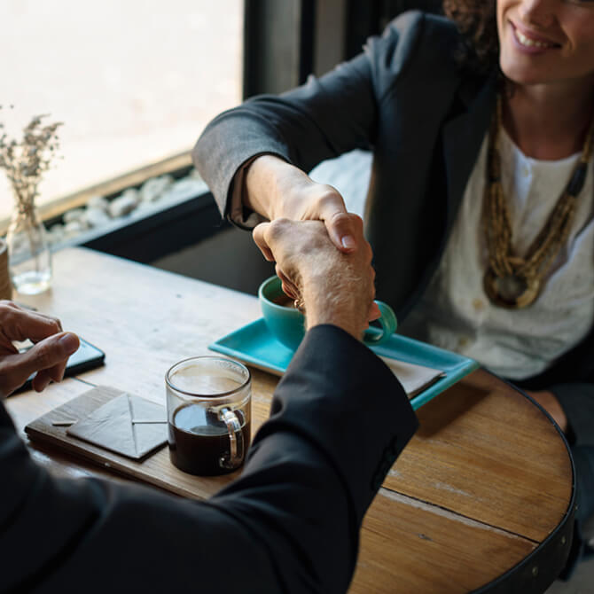 Greybox Investments, businesswoman shaking man's hand while sitting at a table for coffee